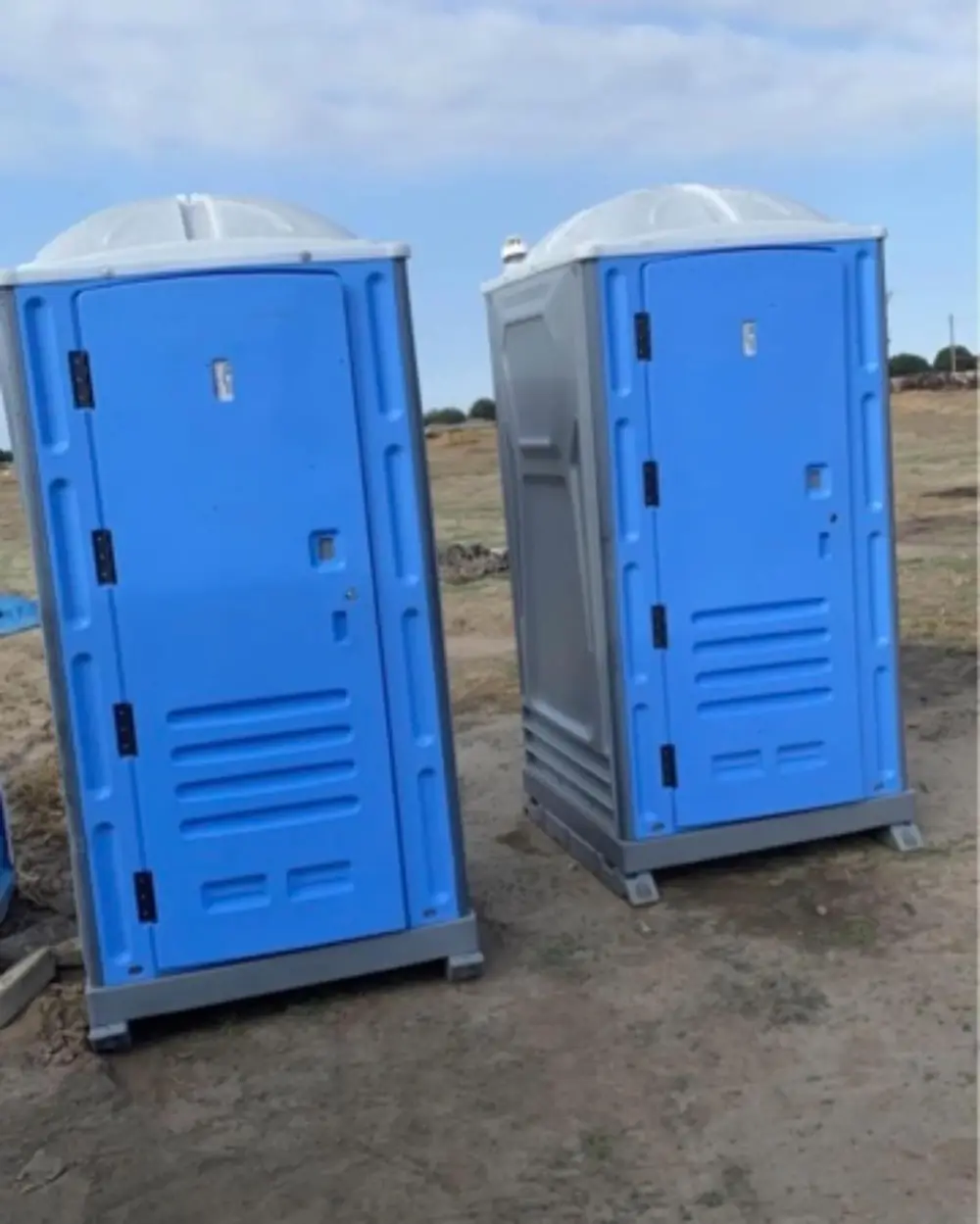 Two portable toilets on a dirt building lot